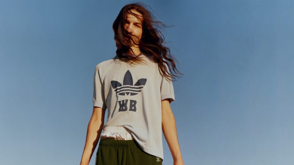 Model in cream adidas Originals Wales Bonner t-shirt with logo against blue sky