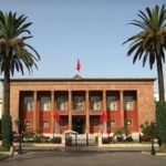 Parliament of Morocco with red-orange facade, red flags, and palm trees