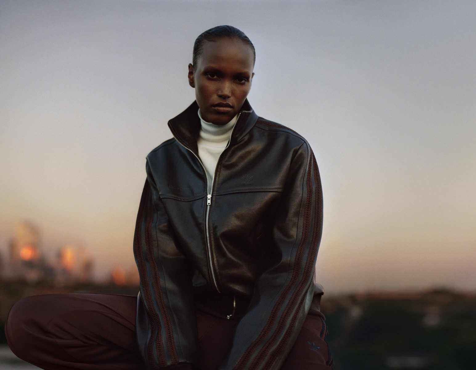 Model in black leather jacket against urban sunset backdrop