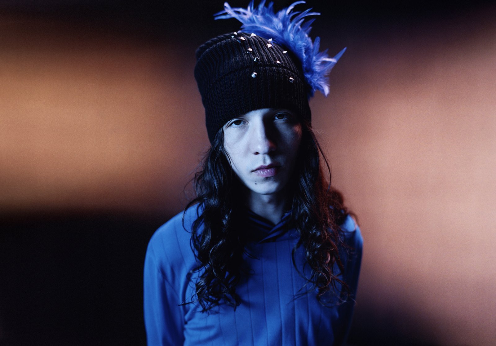Model wearing blue beanie and blue clothing against neutral background