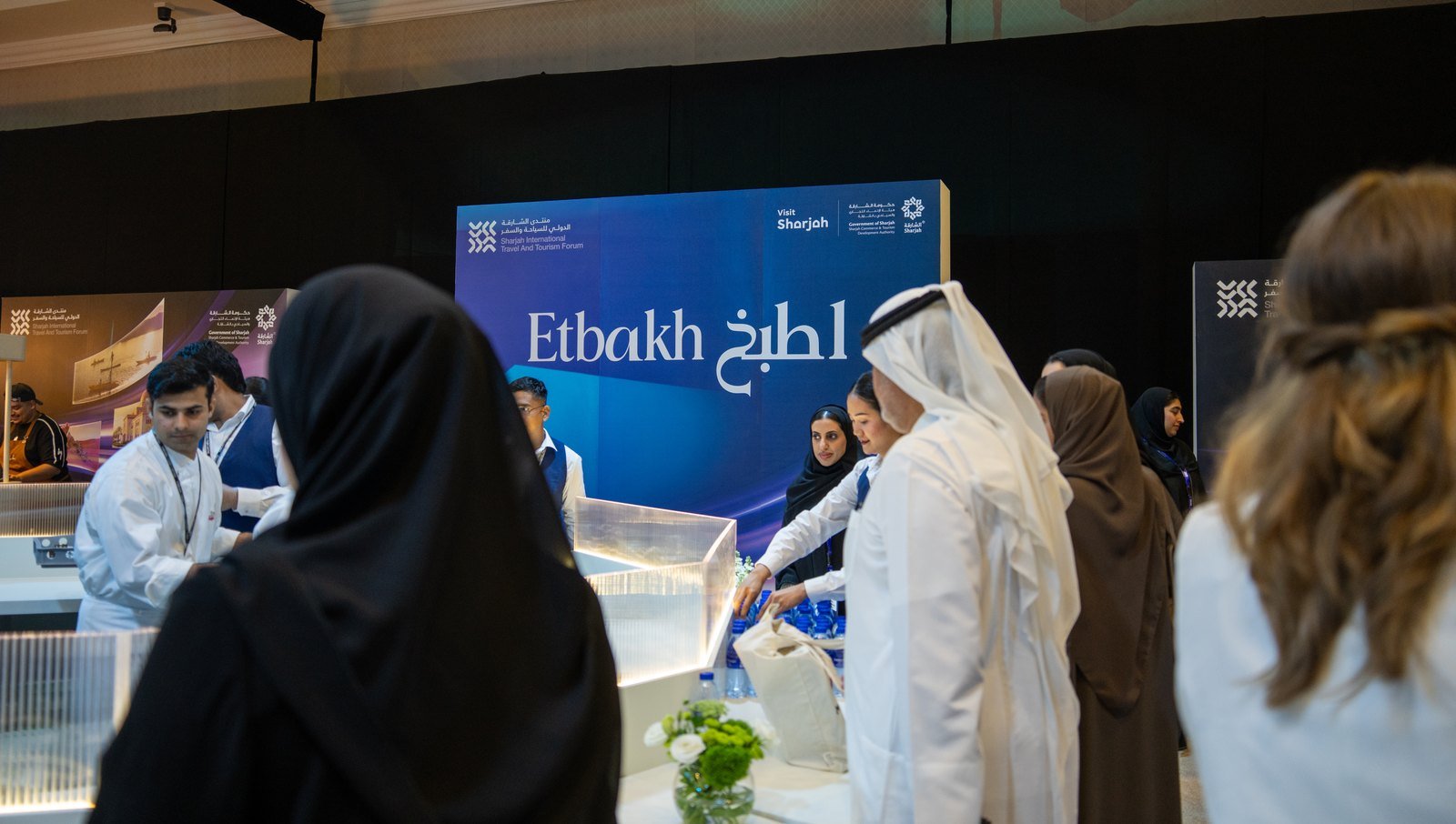 Visitors in traditional and modern dress explore the blue Etbakh exhibition booth