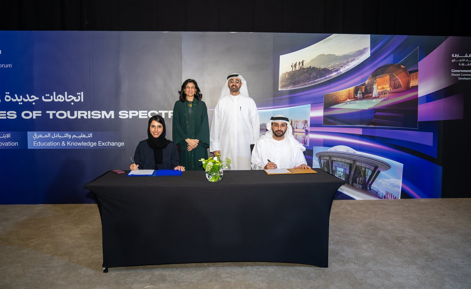 Four people signing agreement at official ceremony table with digital tourism backdrop display