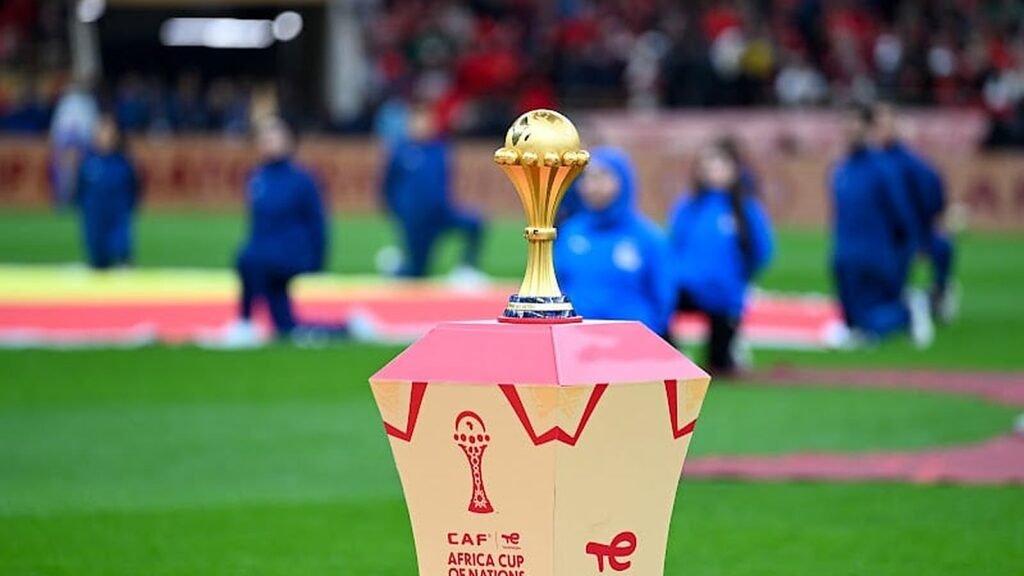 Le trophée doré de la Coupe d'Afrique au centre d'un stade avec des joueurs en arrière-plan