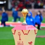 Le trophée doré de la Coupe d'Afrique au centre d'un stade avec des joueurs en arrière-plan