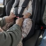 A parent's hands buckling a child into a car seat