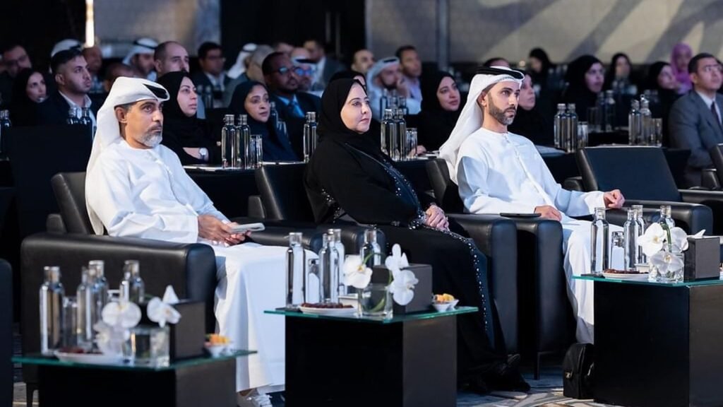 Three officials seated in front rows of Financial Data Forum with attendees visible in background