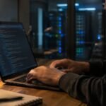 Hands typing on a computer keyboard in a dim technical office