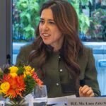 امرأة بملابس رسمية خضراء تتحدث على منصة مع زهور ملونة