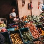 Puesto de mercado con vendedor, zanahorias, tomates y cestas de productos frescos