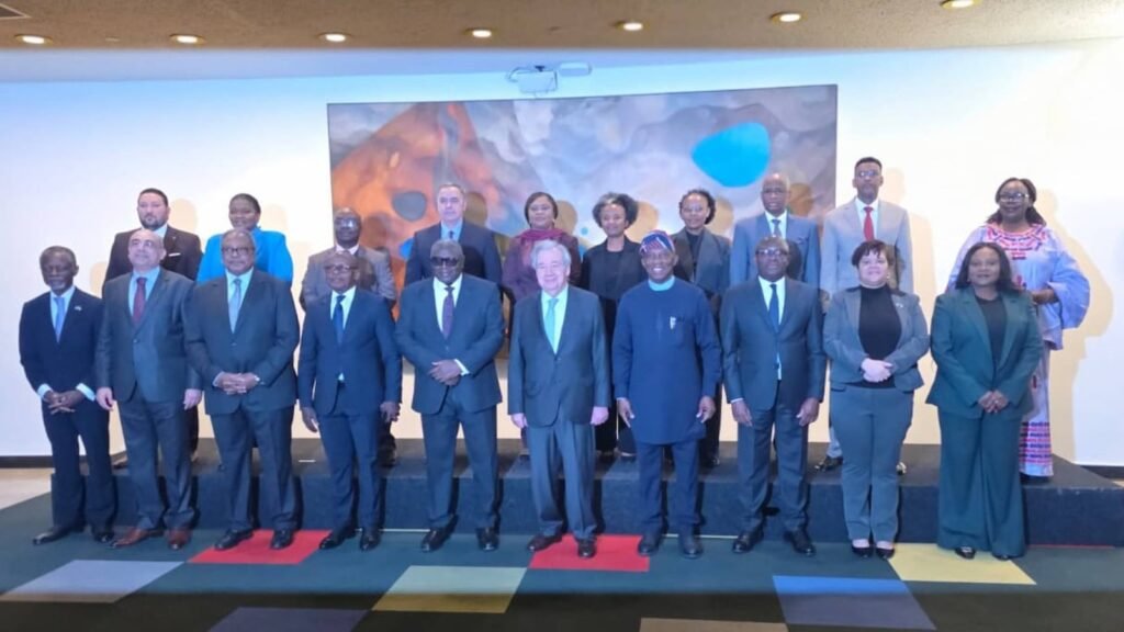 Grupo de funcionarios de pie en una plataforma durante una reunión multilateral con telón de fondo colorido
