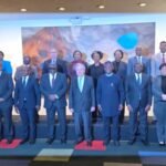 Groupe de responsables debout sur un podium lors d'une réunion multilatérale avec panneau coloré en arrière-plan