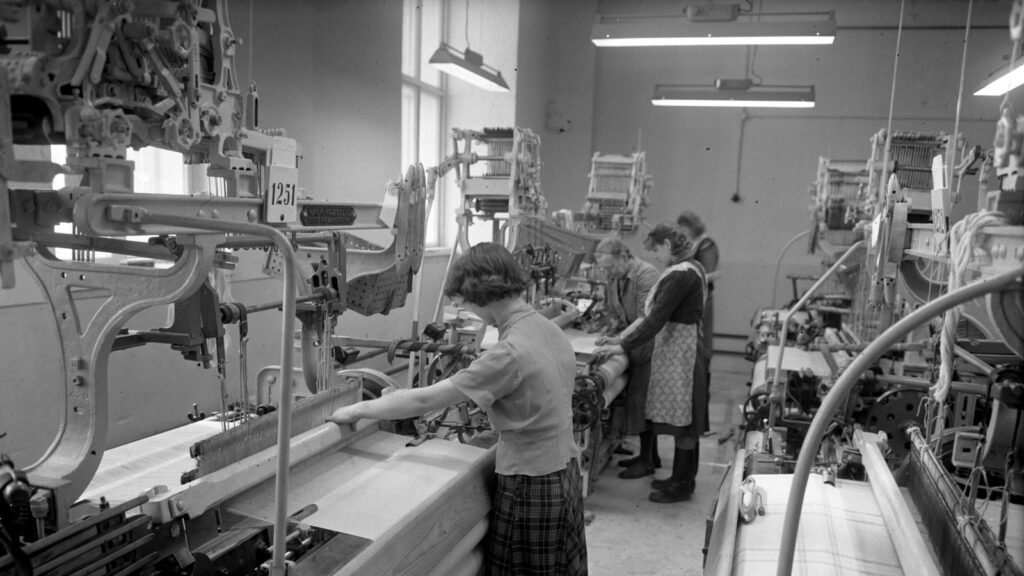 Black and white photo of textile factory workers operating production machinery