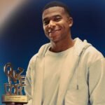 Smiling player holding bronze trophy at awards ceremony with blue backdrop