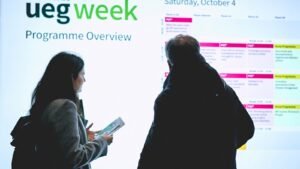 Deux participants debout devant l'écran du programme d'UEG Week, l'un tenant un document imprimé