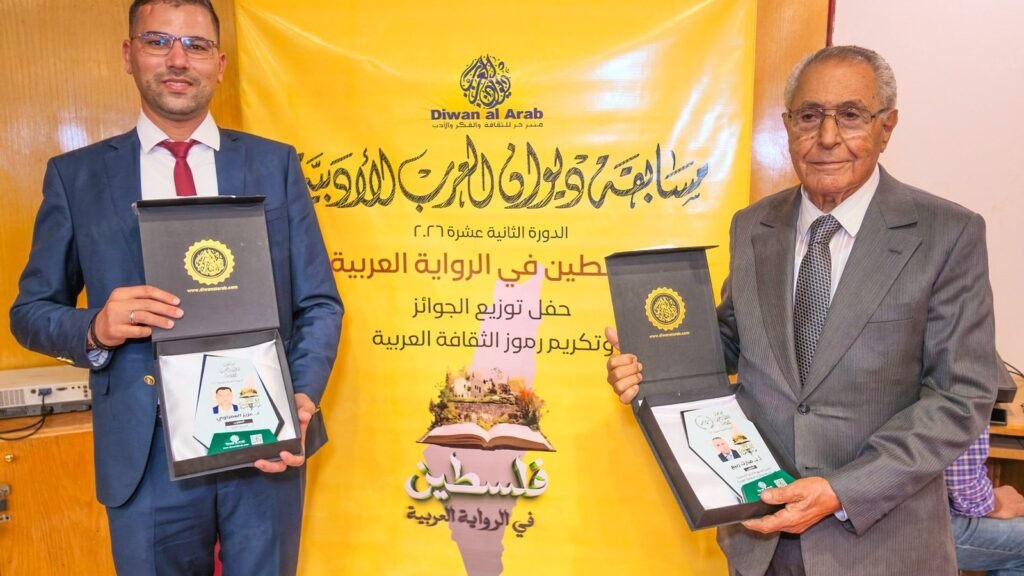 Dos hombres con premios ante el estandarte amarillo del evento Diwan al-Arab