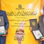 Dos hombres con premios ante el estandarte amarillo del evento Diwan al-Arab