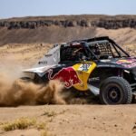 Rally car with Red Bull branding racing through dusty Moroccan desert landscape
