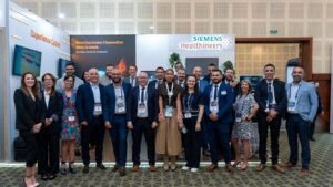Grupo de profesionales en traje formal con credenciales frente a pancarta Siemens Healthineers