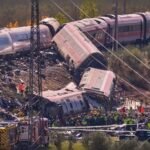 Plusieurs voitures de train rouges et blanches renversées entourées de débris avec équipes de secours