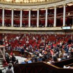 French National Assembly chamber with lawmakers seated in red benches during parliamentary session
